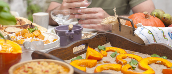 Sweet, baked pumpkin and pie with pear. Autumn dinner for the whole family. Male hands with a glass of wine in the frame. Copy space.