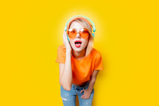 Young style girl with orange glasses and headphones on yellow background. Clothes in 1980s style