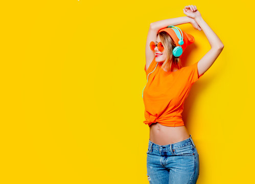 Young style girl with orange glasses and headphones on yellow background. Clothes in 1980s style