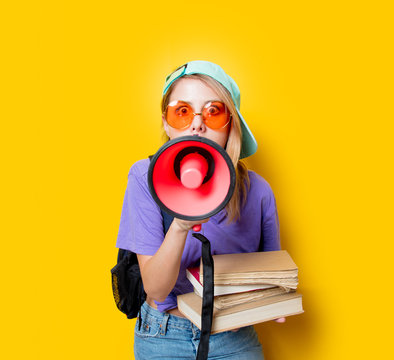 Young style girl in purple clothes with pink megaphone and books on yellow background. Symbolizes female resistance. Clothes in 1980s style