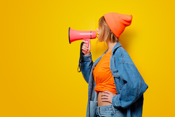 Young style girl in jeans clothes with pink megaphone on yellow background. Symbolizes female resistance. Clothes in 1980s style - obrazy, fototapety, plakaty