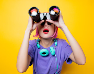 Young style girl in purple clothes with binoculars on yellow background.  Clothes in 1980s style
