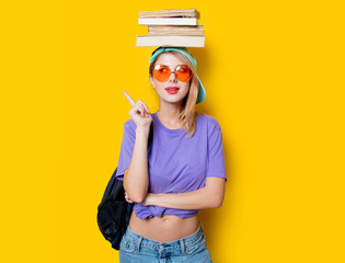 Young style student girl with orange glasses and books on yellow background. Clothes in 1980s style