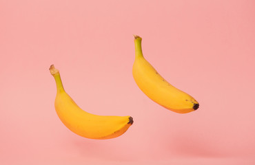 Two yellow bananas levitate in air on pink background.
