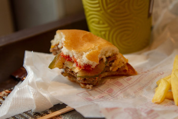 The leftovers of lunch in McDonald's. The Doublecheese menu with coffee latte and French fries on the McDonald's signature wrapper. Lunch of freelancer. Close-up.