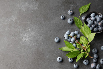 Fresh blueberries with leaves on branch. Black stone background, top view.