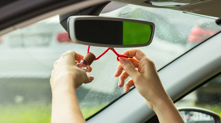 A woman's hand knots an air freshener on a mirror, close-up