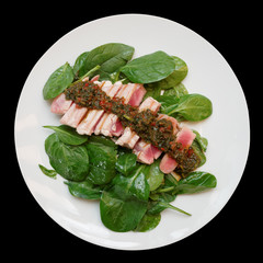Grilled tuna with spinach and chimichurri sauce isolated on black