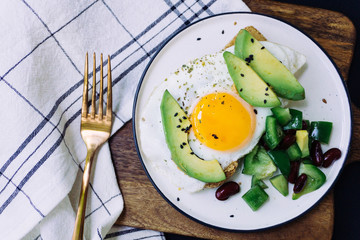 A healthy breakfast of toast with avocado, whole wheat bread and fried egg and burrito salad on white plate. Top view