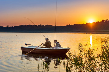 father and son catch fish from a boat at sunset - 215565424