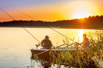 father and son catch fish from a boat at sunset - 215565444