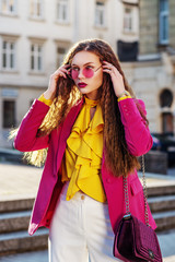 Outdoor fashion portrait of young beautiful woman wearing stylish round pink sunglasses, fuchsia...