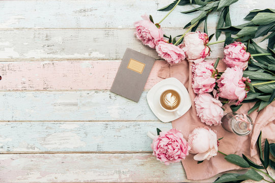 Flat lay cup of coffee and peonies on shabby chic background.