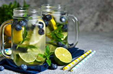 Lemonade with lime, lemon and blueberries on a stone background. Summer cold drink.