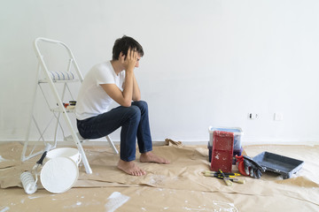 Painting Equipment in the room and discouraged young man having problems with renovations