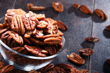 Bowl with pecan nuts on wooden table.