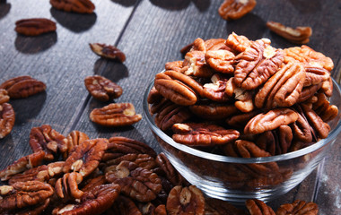 Bowl with pecan nuts on wooden table.