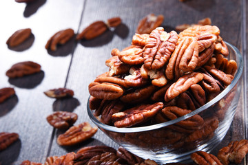 Bowl with pecan nuts on wooden table.