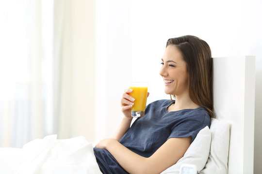 Happy woman on a bed holding an orange juice