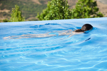 Young woman relaxing in infinity swimming pool looking at nature landscape on background, outdoor