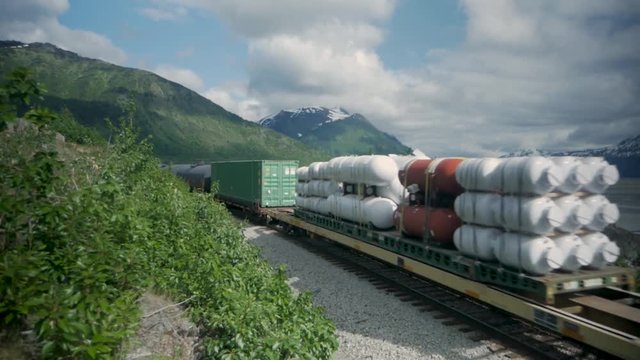 An Alaska Railroad cargo train passes by along Seward Highway in Alaska, with snow-capped mountains in the background.