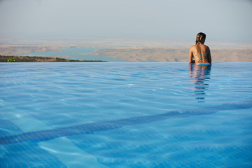 Young woman relaxaing in the swimming pool looking at the nature landscape view on background. Travel, summer holiday concept