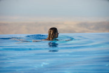 Fototapeta premium Young woman relaxaing in the swimming pool looking at the nature landscape view on background. Travel, summer holiday concept