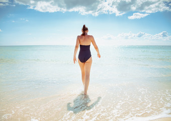 modern woman in swimsuit on seashore going into sea