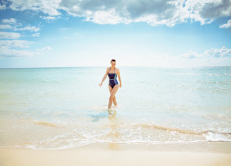 Fototapeta na wymiar smiling modern woman in beachwear on seashore come out of sea