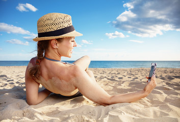smiling modern woman taking selfie with cellphone on seacoast