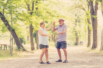 Naklejka na ściany i meble Happy smiling senior couple in love, dancing and having fun in the park. Being together, in love, retirement happy life concept.