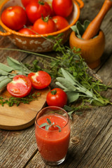 Glass of fresh tomato juice with herbs on the wooden table. Healthy organic nutrition concept.
