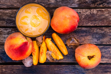 Glass of peach juice and peaches on wooden table