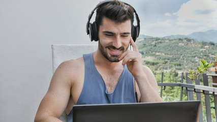 Waist Up Profile of Attractive Man with Dark Hair, Sitting with Laptop Computer Listening to Music with Big Headphones
