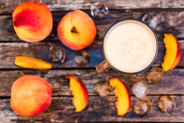 Glass of peach yoghurt and peaches on wooden table