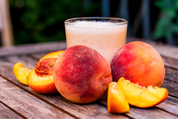 Glass of peach yoghurt and peaches on wooden table