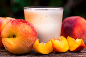 Glass of peach yoghurt and peaches on wooden table