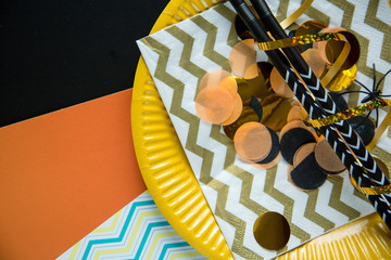 Flat lay style of halloween party concept with decorative confetti, plates and black fancy straw on...