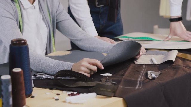 Close-up of a hands of tailores fashion designers working with gray material using sketches, they sitting at the beautiful atelier with different tailoring tools and clothes. Tailor and dressmaker