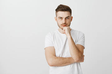 Studio shot of intense unsure stylish male model with cool hairstyle in white t-shirt frowning...