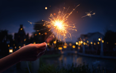 Hand holding a sparkler with neighborhood background