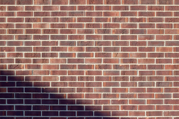 Traditional running bond pattern brown brick wall background with encroaching shade in lower left angle