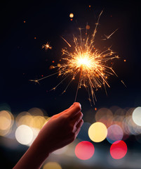 Hand holding a sparkler with blurred busy city light