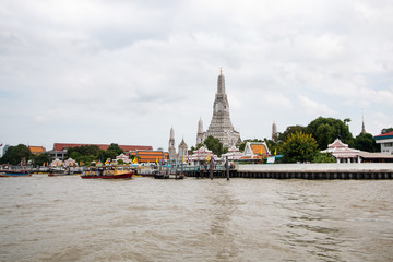 Obraz premium Wat Arun buddhist temple . famous ancient grand palace in Bangkok Thailand , asian travel landmark . old historic architecture . Chao phraya river with boats . beautiful clear sky and clouds