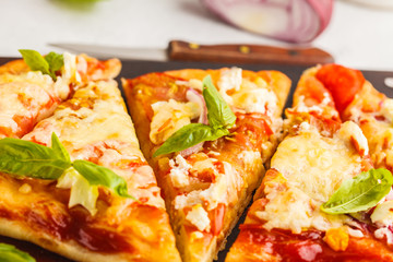Oval homemade pizza with feta cheese, tomatoes and basil on a wooden board.