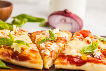 Oval homemade pizza with feta cheese, tomatoes and basil on a wooden board.