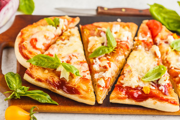 Oval homemade pizza with feta cheese, tomatoes and basil on a wooden board.