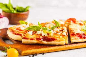 Oval homemade pizza with feta cheese, tomatoes and basil on a wooden board.