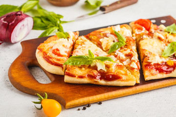 Oval homemade pizza with feta cheese, tomatoes and basil on a wooden board.