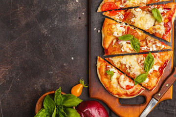 Oval homemade pizza with feta cheese, tomatoes and basil on a wooden board.